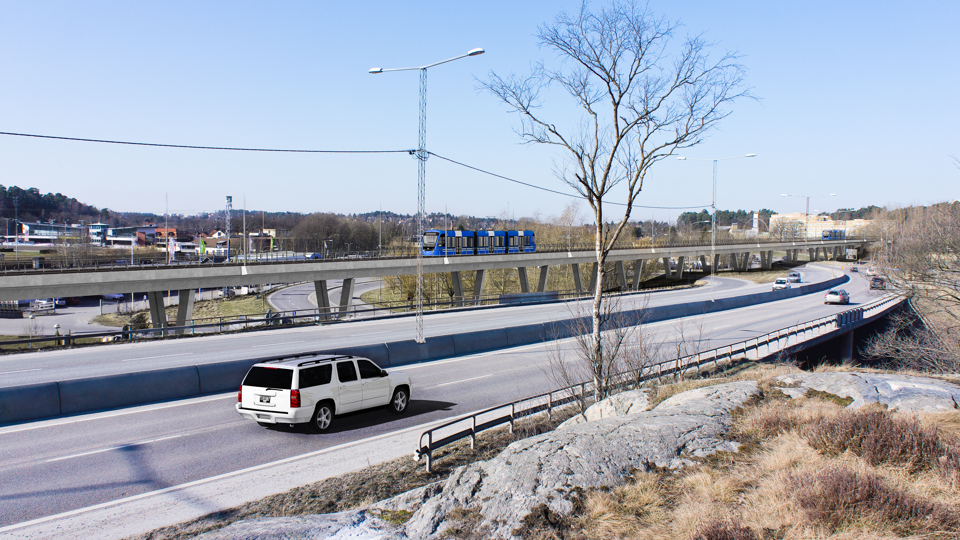 En bro för bilar och en bro för tvärbanan, över Bällstavägen. Bilar och tvärbanetåg syns på bilden och omgivningar med träd, vägar, hus. Foto